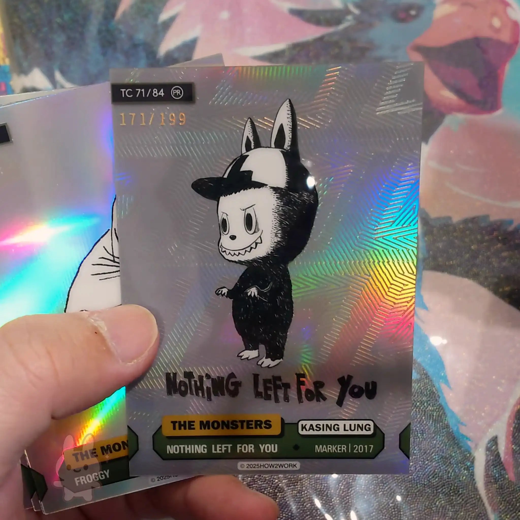 Holographic trading card with a cartoon character and text, held by a hand against a colorful background.