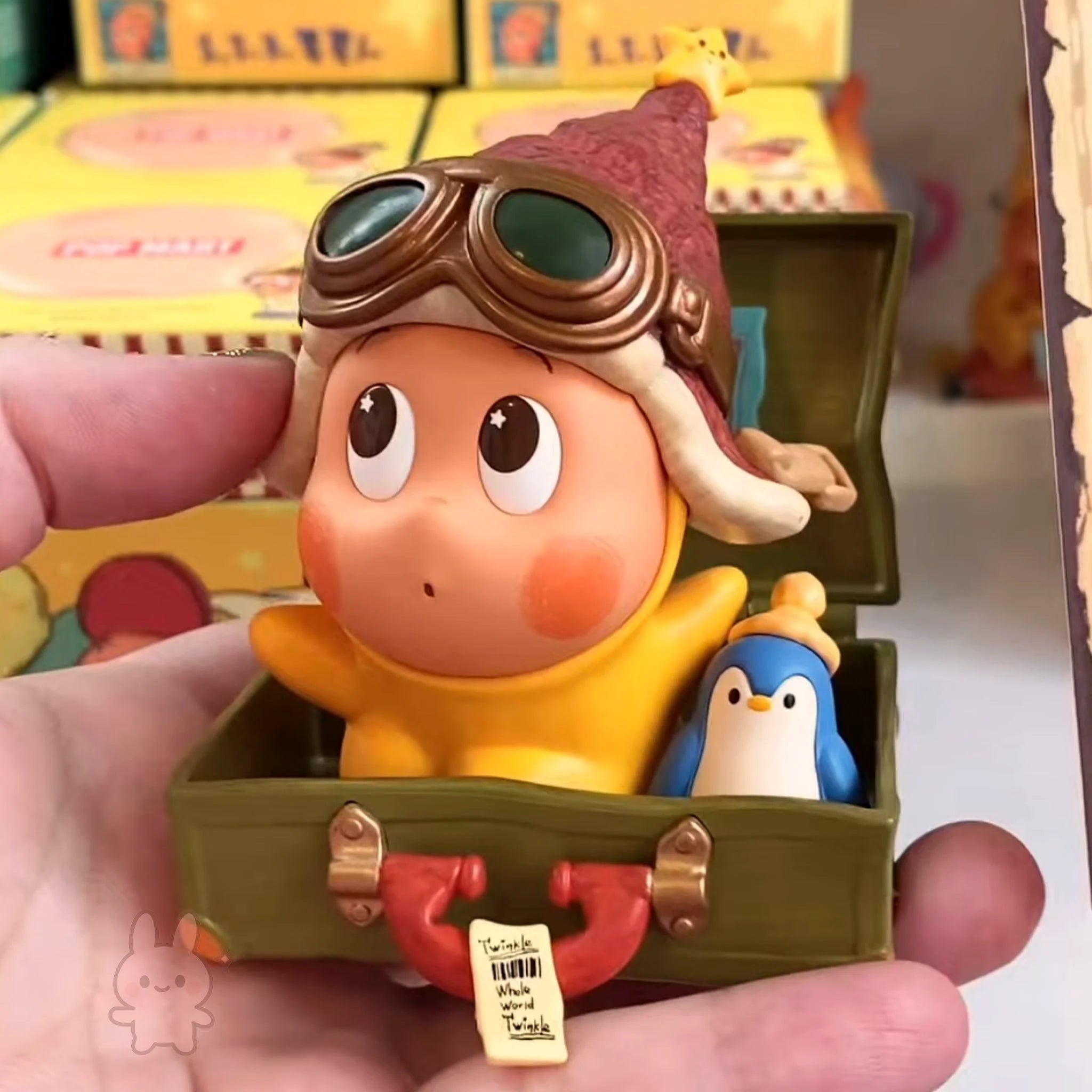Twinkle Twinkle Be a Little Star Toy figure of a character with goggles and a penguin inside a suitcase, held in a hand.