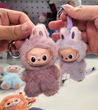 Plush keychains shaped like cartoon characters with bunny ears held by hands.