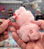 Pink plush toy with a keychain attachment held by hands against a blurred background of toys.