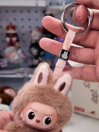 Plush keychain with cartoon face held by a hand against a blurred background