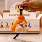 Plush keychain with a character in front of a 'Cheer Up Baby!' box.