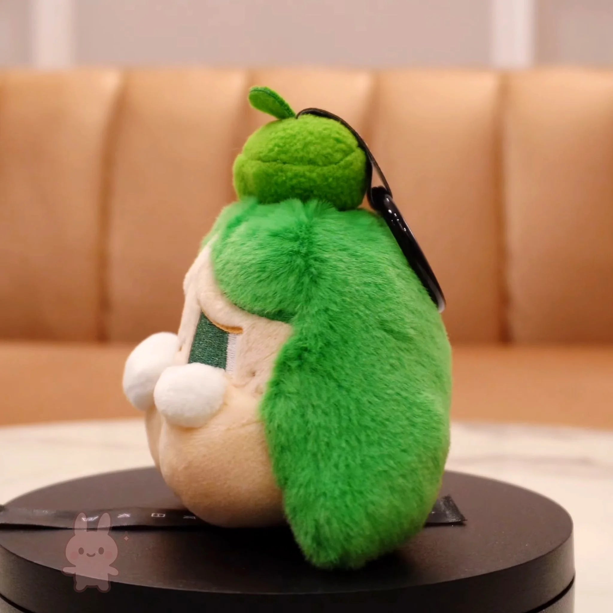 Plush toy shaped like a character with green fur and beige face on a round black platform.