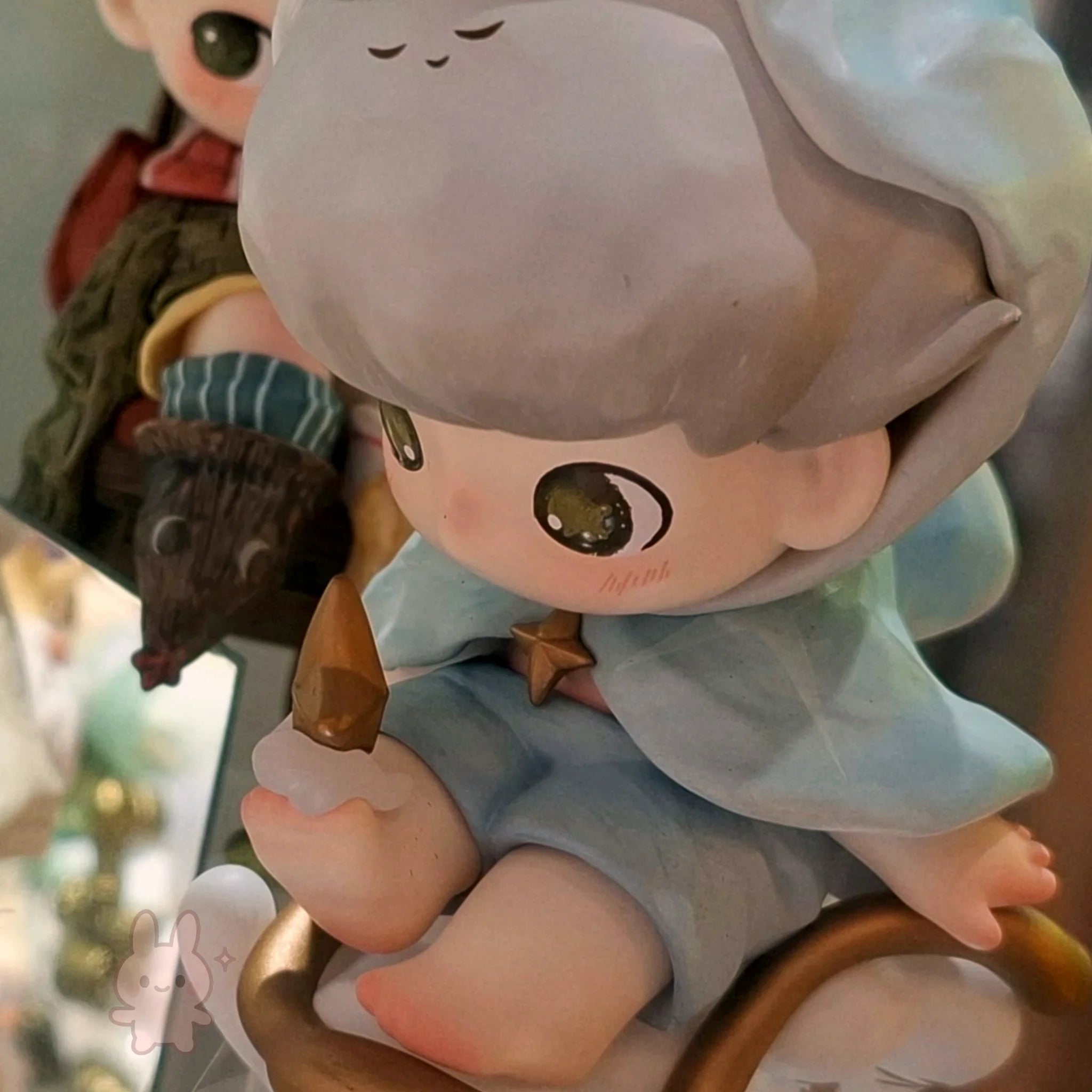 dimoo-the-missing-day Detailed figurine of a character with a gray hat and blue dress, holding a small creature.
