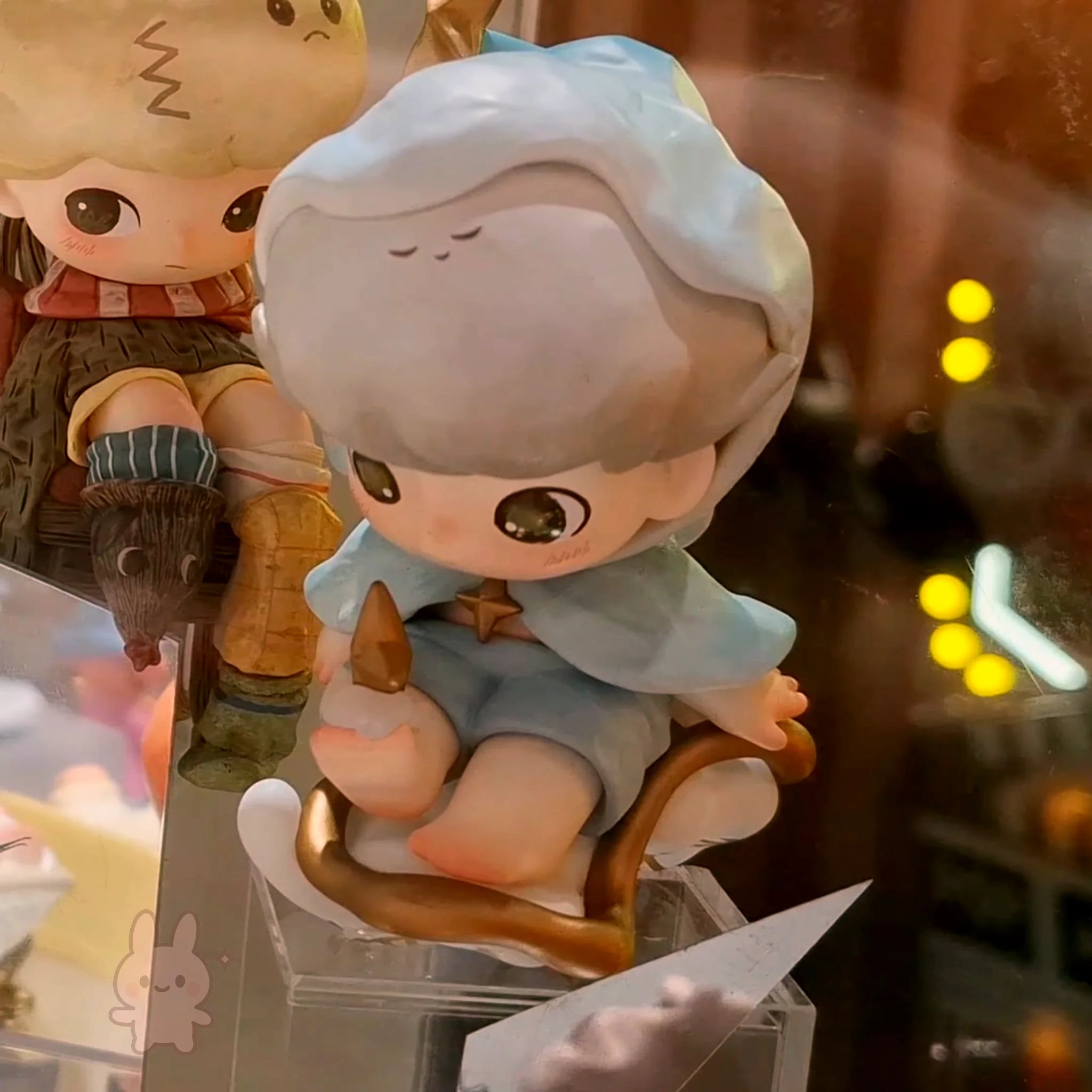 dimoo-the-missing-day Small figurine of a character with a hat and outfit, sitting on a wooden stool.