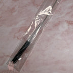 Cleaning brush with black bristles in clear packaging on a pink marble background