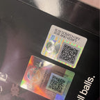 Two holographic security labels with QR codes on a reflective surface.