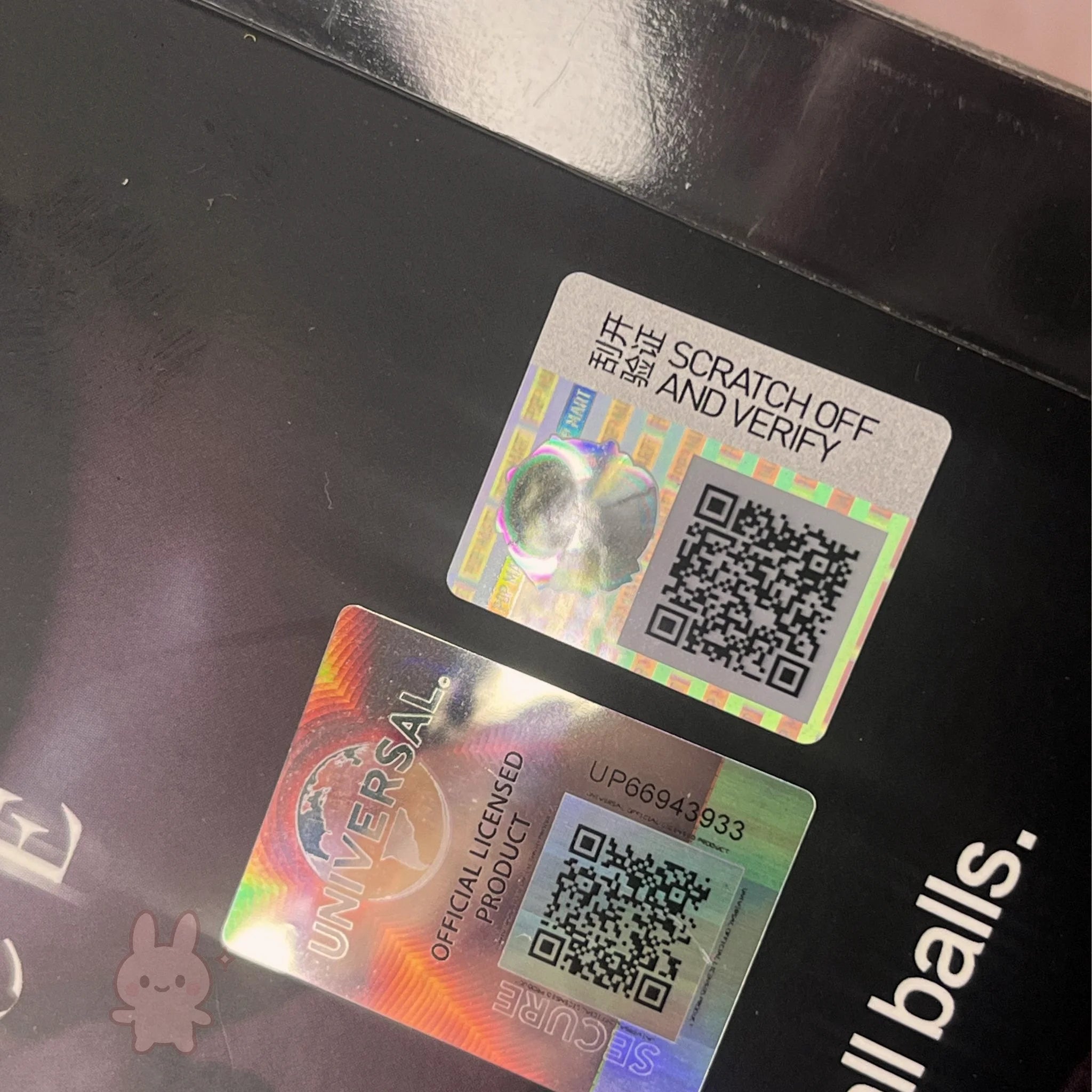 Two holographic security labels with QR codes on a reflective surface.