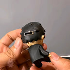 Hand holding a small hirono black and gray figurine against a neutral background
