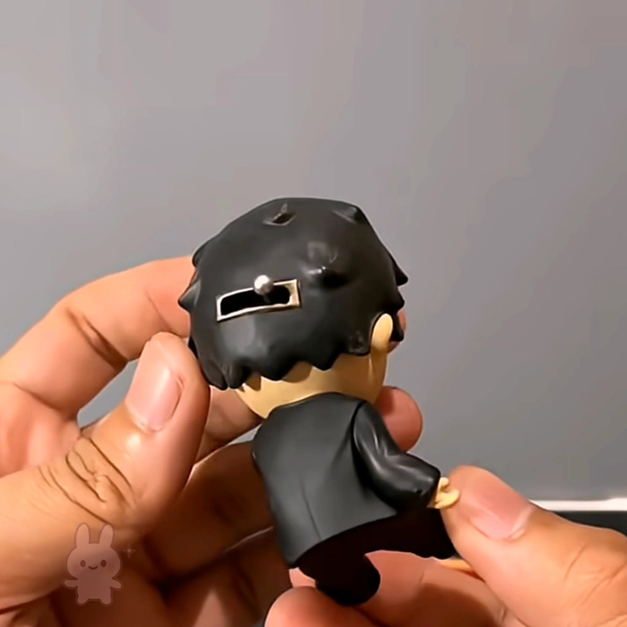 Hand holding a small hirono black and gray figurine against a neutral background