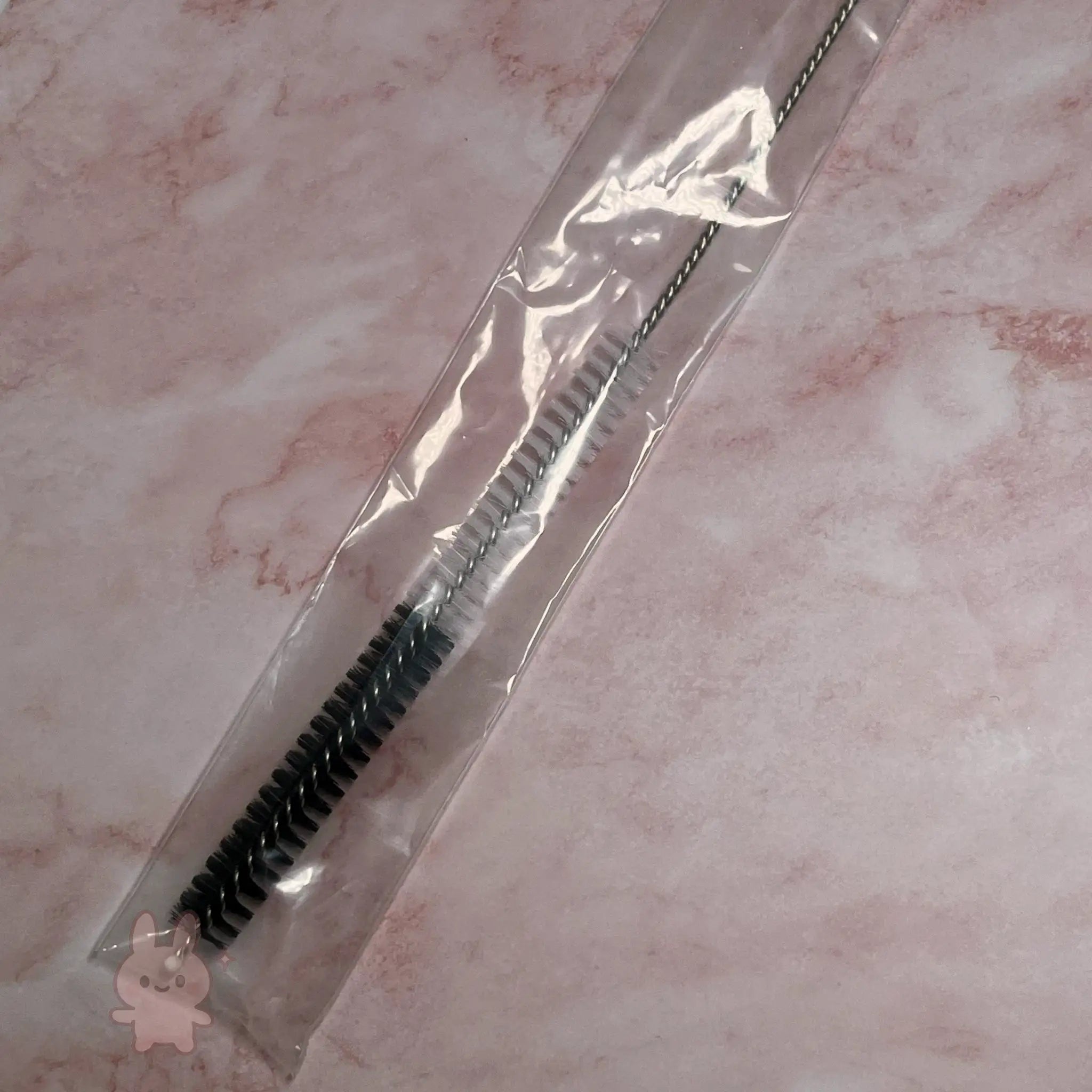 Cleaning brush with black bristles in clear packaging on a pink marble background