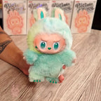 labubu-big-into-energy Plush toy with green and pink fur held by a person on a wooden surface, with 'Big Head Baby' boxes in the background.