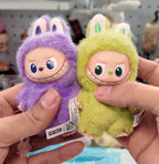 Labubu Two plush toys, one purple and one green, held by a person with a blurred store background.