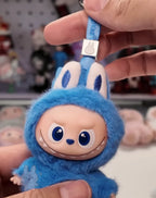 Labubu Blue plush keychain with a smiling face held by a hand against a blurred background