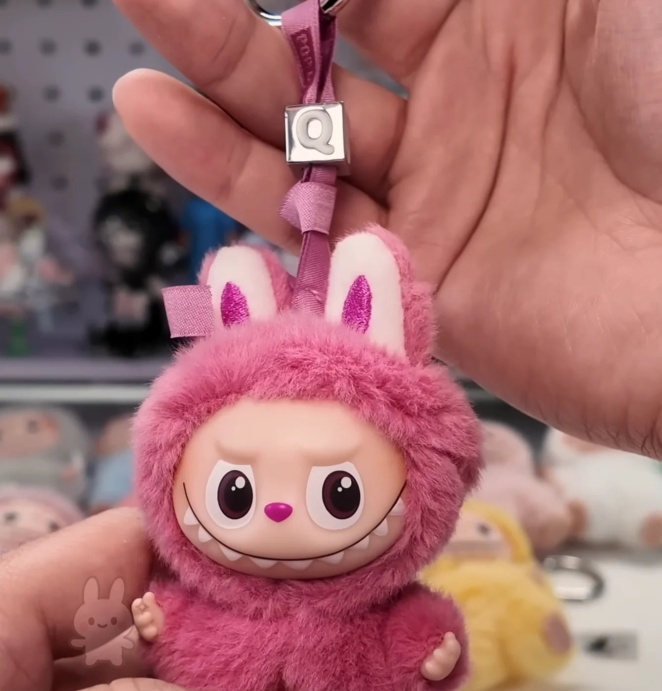 Pink plush keychain with a face held by a hand against a blurred background