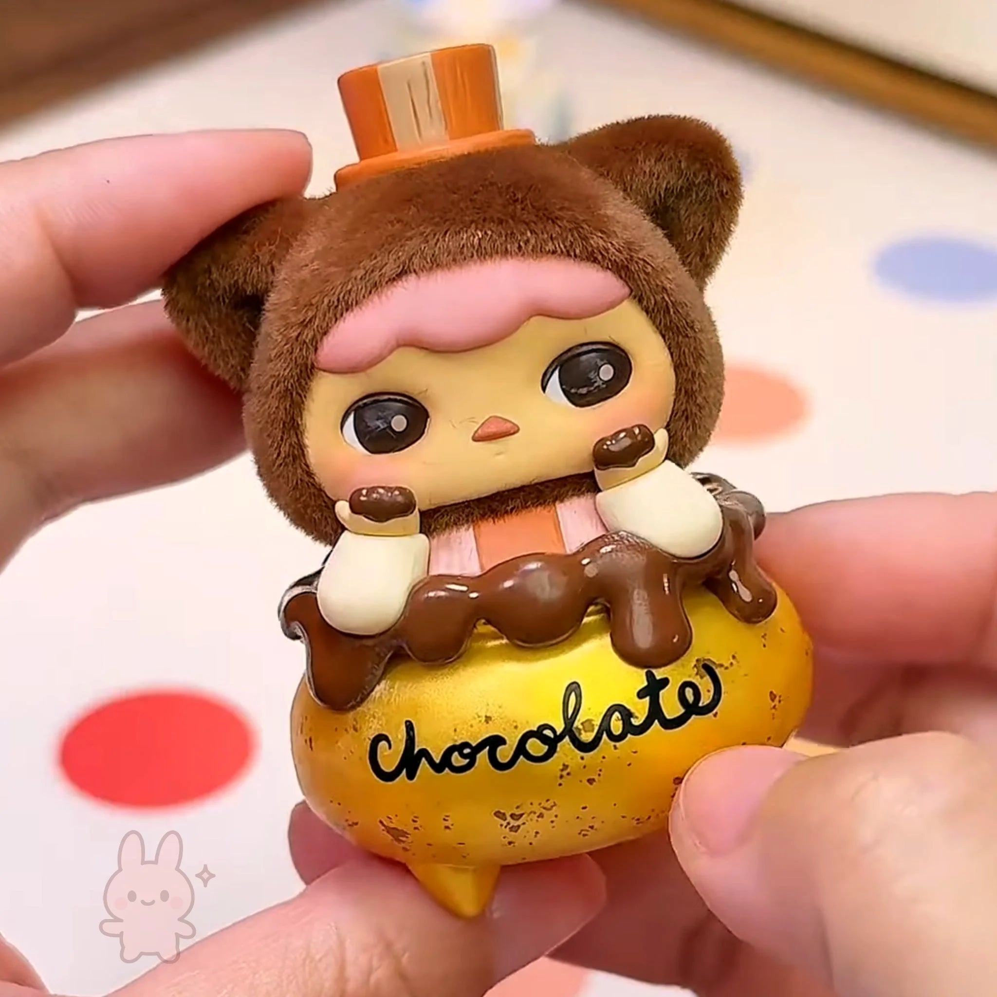 pucky faries market Cute figurine of a bear with chocolate on a yellow base held by hands.