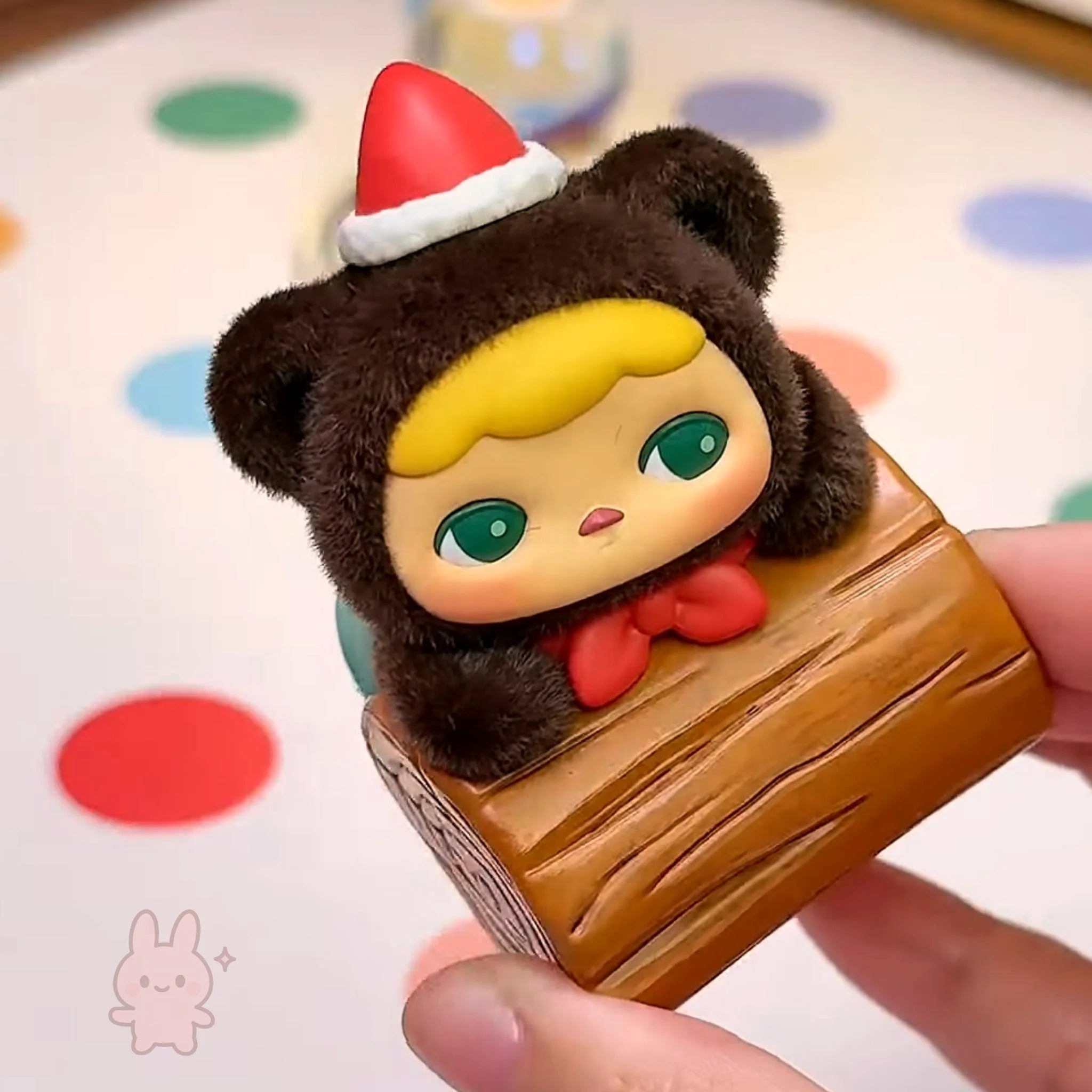 pucky faries market Small figurine of a bear character with a Santa hat on a wooden block, held by a hand.