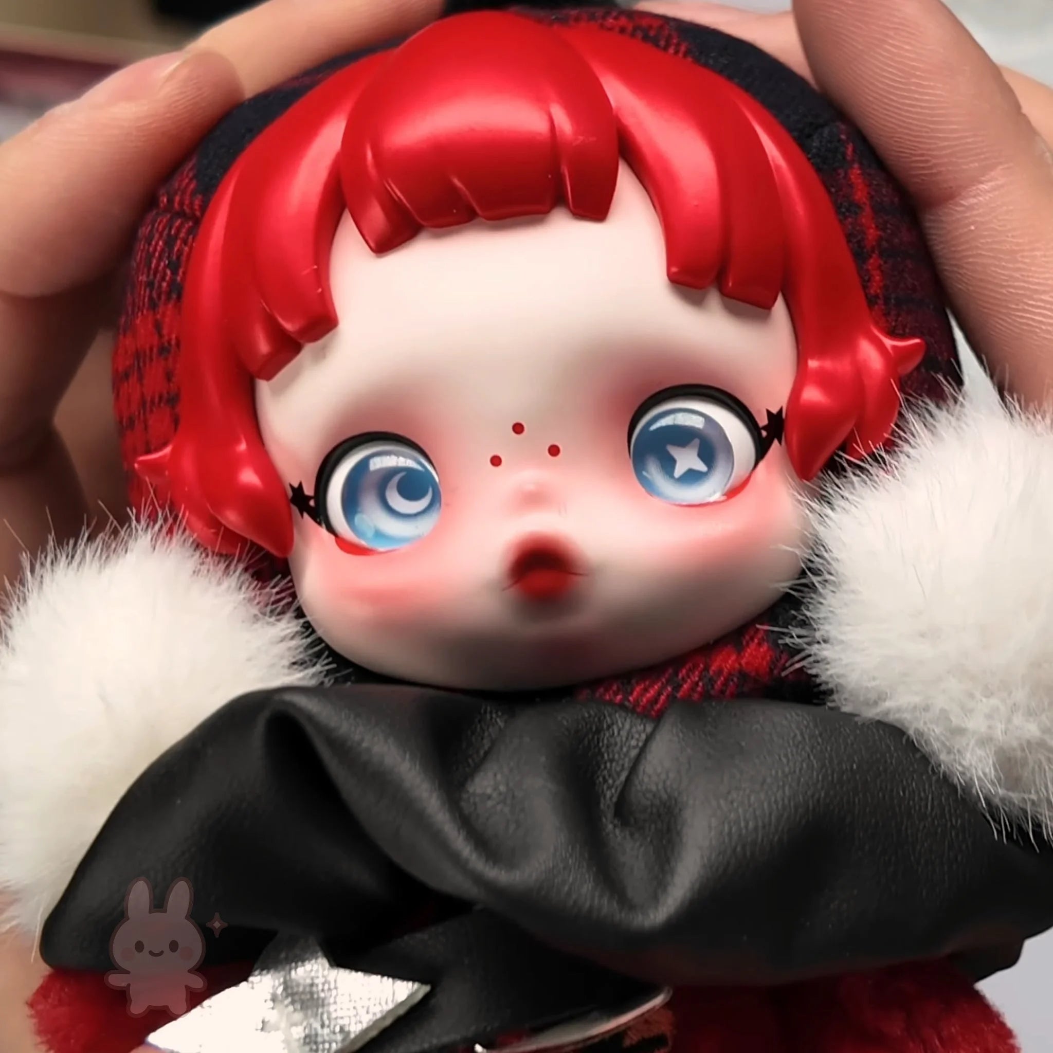 skullpanda Toy figure with red hair and blue eyes held by a hand