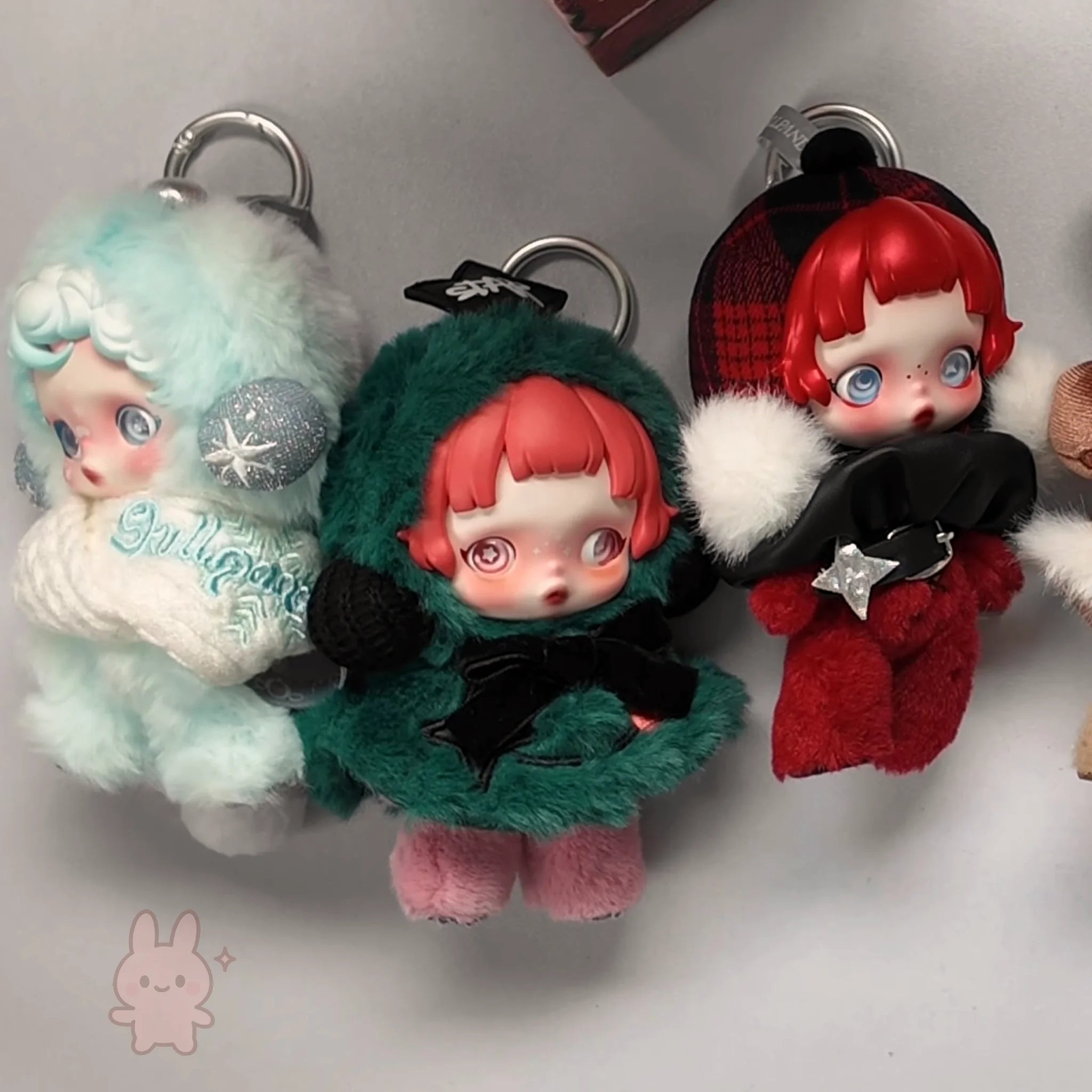 skullpanda Three plush keychains with doll-like faces on a light gray background