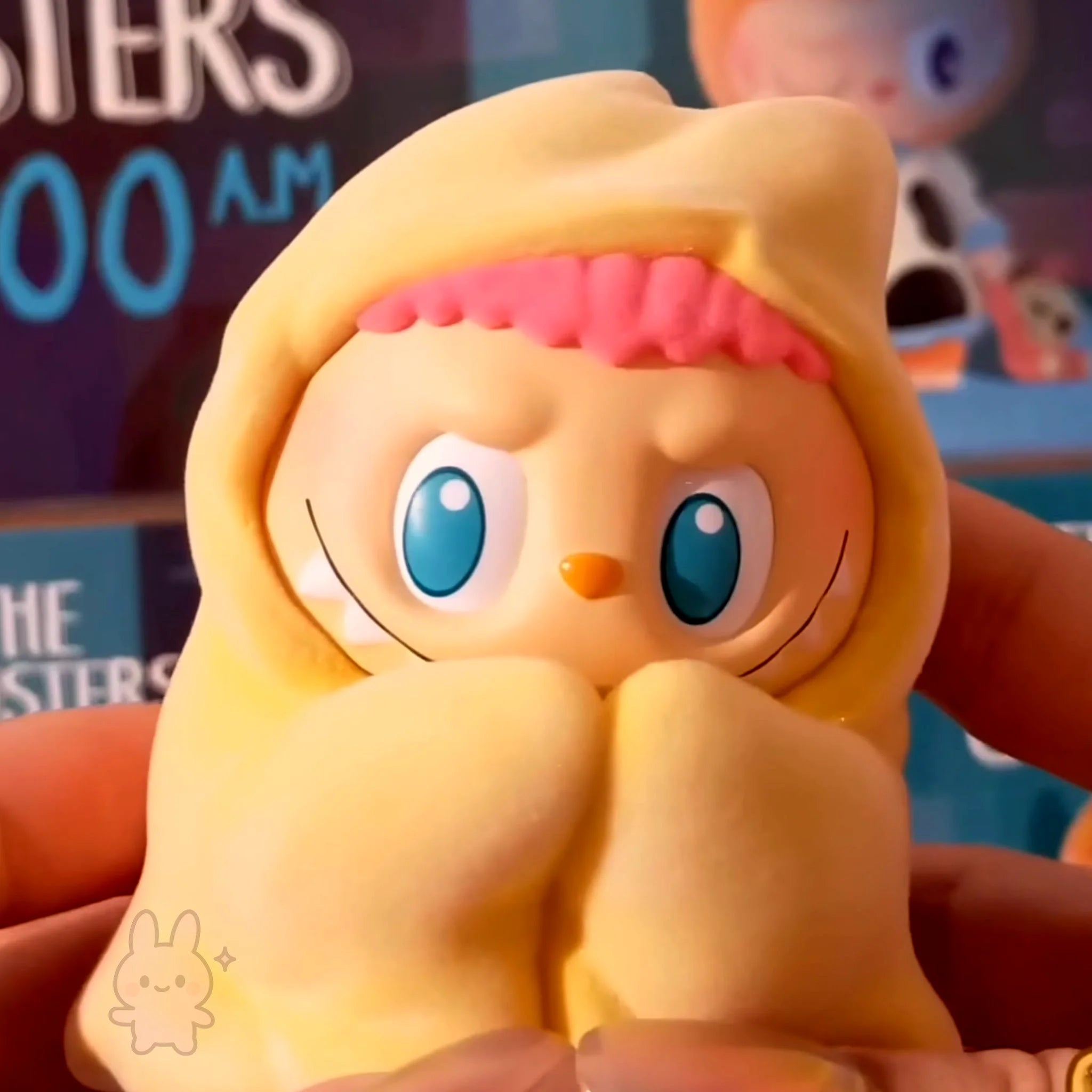 the-monster-1am-series Yellow cartoon character with blue eyes and pink hairband held by a hand.