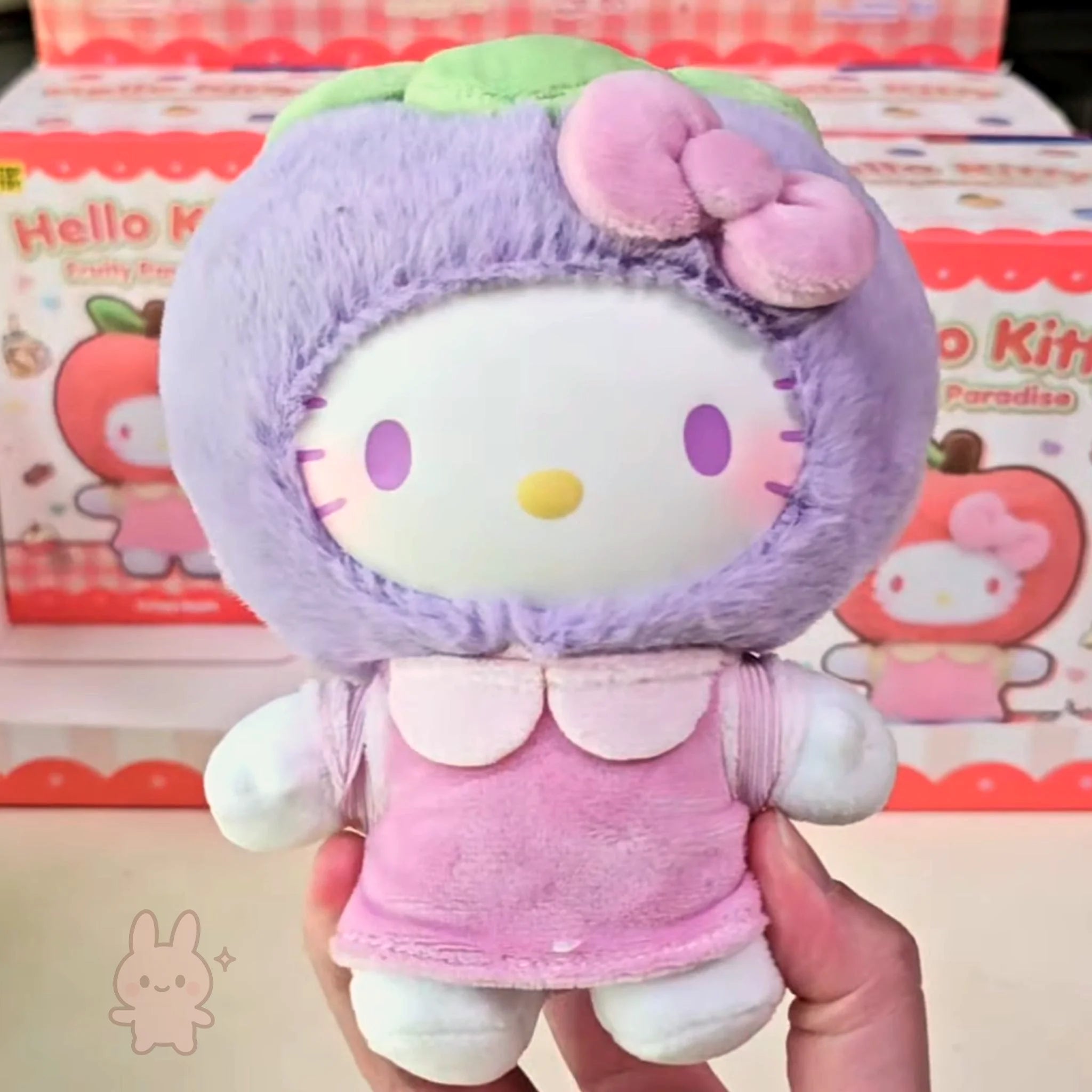 hello kitty Plush toy resembling a character with a purple outfit and pink accents, held in front of Hello Kitty packaging.