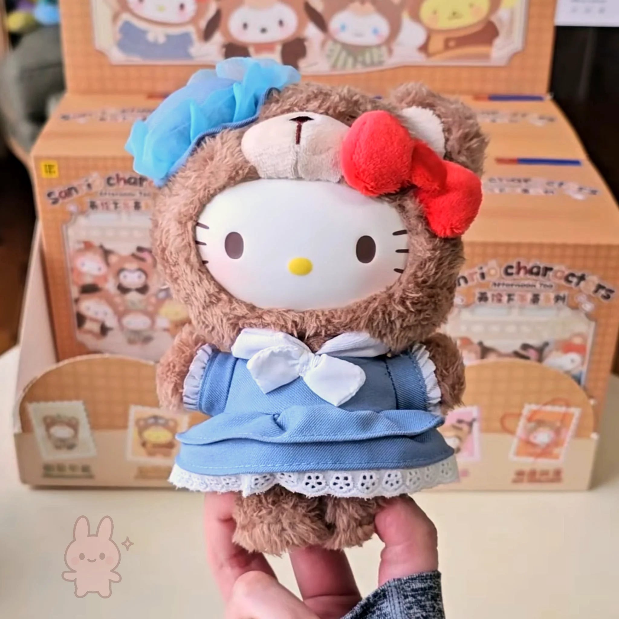 sanrio-afternoon Plush toy resembling a character with a blue bow and red flower, held in front of a box with cartoon characters.