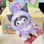 Sanrio characters Elf Bunny Baby Plush keychain with cartoon character in a purple outfit held by a hand, with colorful boxes in the background.