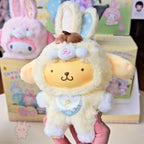 Sanrio characters Elf Bunny Baby Plush toy resembling a lamb with a brown hat held by a hand, with colorful boxes in the background.
